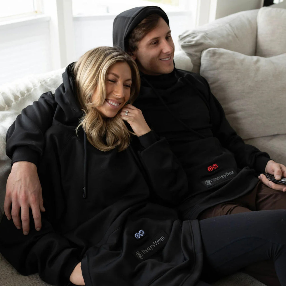 Couple relaxing on a sofa, both wearing the TherapyWear Relief Hoodie